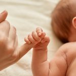 Ilustrasi bayi menggenggam jari orang dewasasimbol kerentanan dan hak anak atas perlindungan sejak awal kehidupan