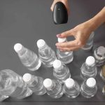 Person uses a handheld barcode scanner to scan a row of plastic water bottles at a checkout or inventory station