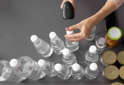 Person uses a handheld barcode scanner to scan a row of plastic water bottles at a checkout or inventory station