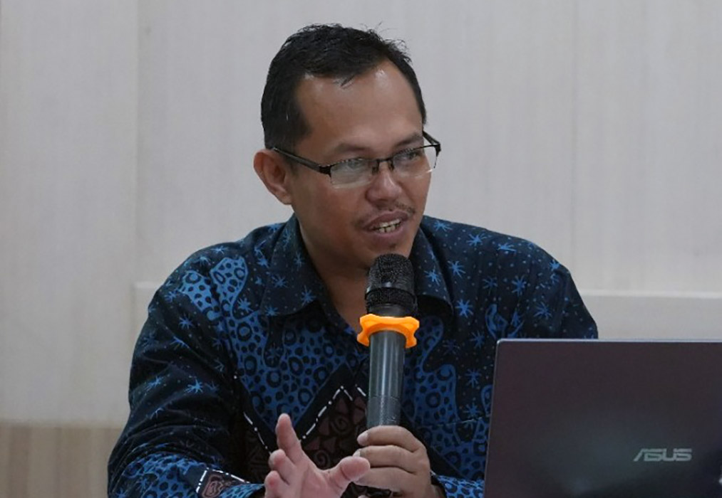 17dham catrawarta Man in glasses speaks into a handheld microphone while seated at a table with an asus laptop nearby