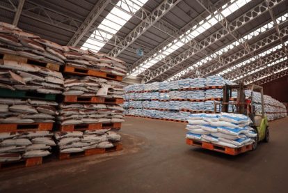 Warehouse with tall pallets stacked with white bags a forklift moves a pallet in the foreground