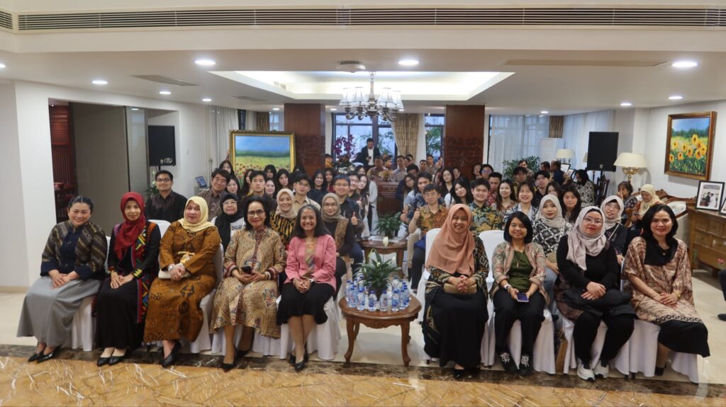 Large group posing for a photo in a formal banquet room many wearing batik front row seated with a chandelier and art behind them
