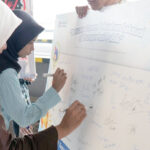 Women in hijabs sign a large banner at an indonesian campaign against sexual harassment in public transportation