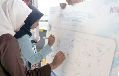 Women in hijabs sign a large banner at an Indonesian campaign against sexual harassment in public transportation.