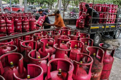 Several workers move and stack red Bright Gas cylinders on and around a flatbed truck in an urban loading area outside.