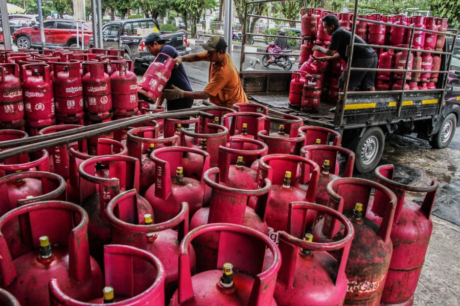 Several workers move and stack red bright gas cylinders on and around a flatbed truck in an urban loading area outside