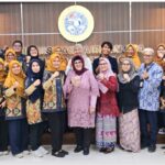 Group of colleagues posing together in traditional batik outfits fist raised in a conference room with a seal backdrop behind them