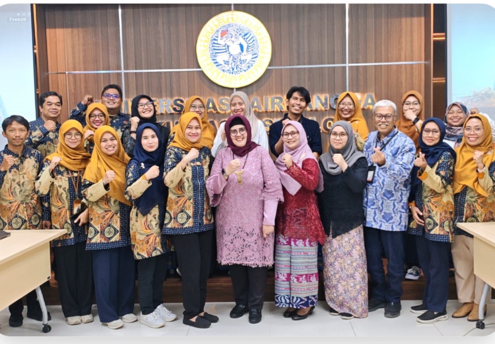 Group of colleagues posing together in traditional batik outfits fist raised in a conference room with a seal backdrop behind them