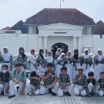 Group of students in matching uniforms posing together on a school trip in front of vredeburg fort The girls wear white hijabs and floral tops while the boys wear matching shirts and white pants