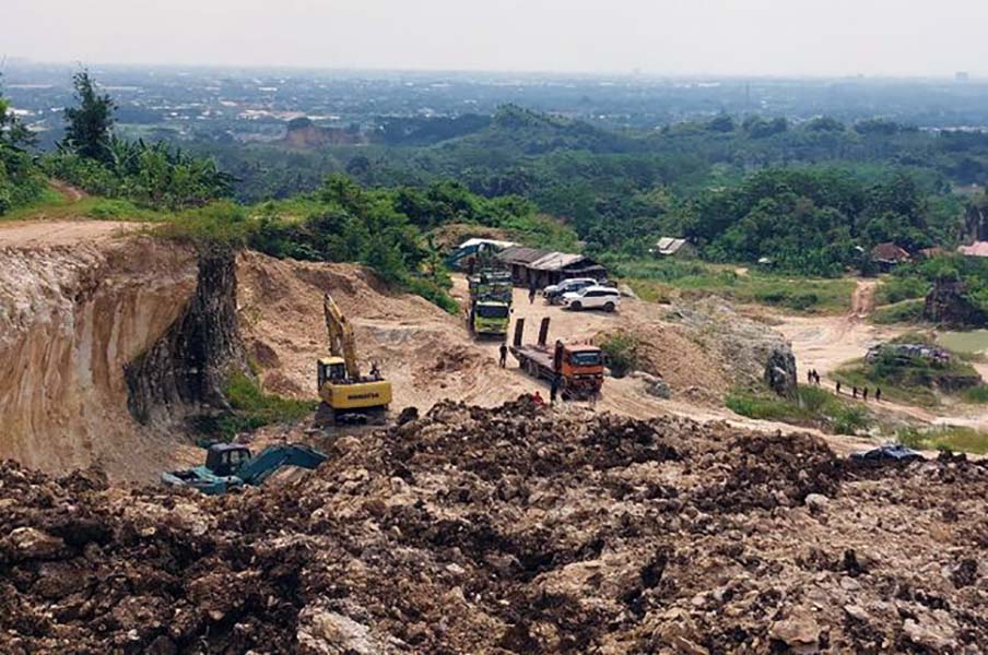 24drusak catrawarta Open pit quarry with excavator and dump trucks on a dirt road brown rocky piles and green hills in the background