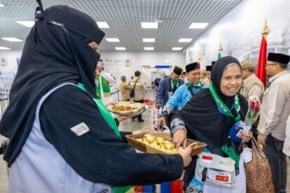 Smiling woman in a black hijab hands a wicker basket of pastries to a guest at an indoor event