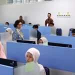 Instructor walking through a computer lab as students sit at blue cubicles working at desks with computers in front of them