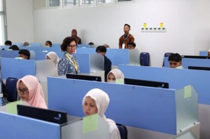 Instructor walking through a computer lab as students sit at blue cubicles working at desks with computers in front of them