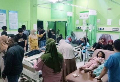 Busy hospital ward with green walls patients on beds connected to ivs surrounded by family and staff