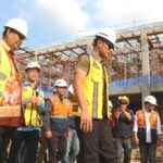 Group of construction workers wearing hard hats and reflective vests on a scaffolding filled construction site with a blue sky behind them