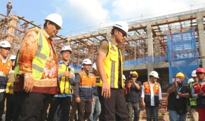 Group of construction workers wearing hard hats and reflective vests on a scaffolding filled construction site with a blue sky behind them