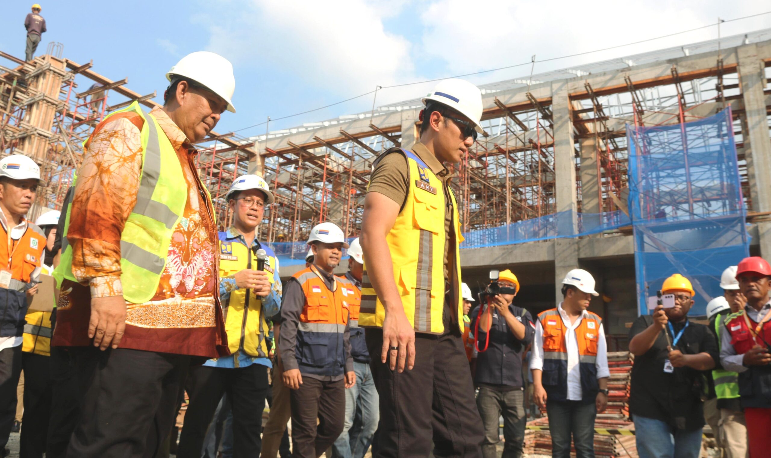 26ayh catrawarta Group of construction workers wearing hard hats and reflective vests on a scaffolding filled construction site with a blue sky behind them