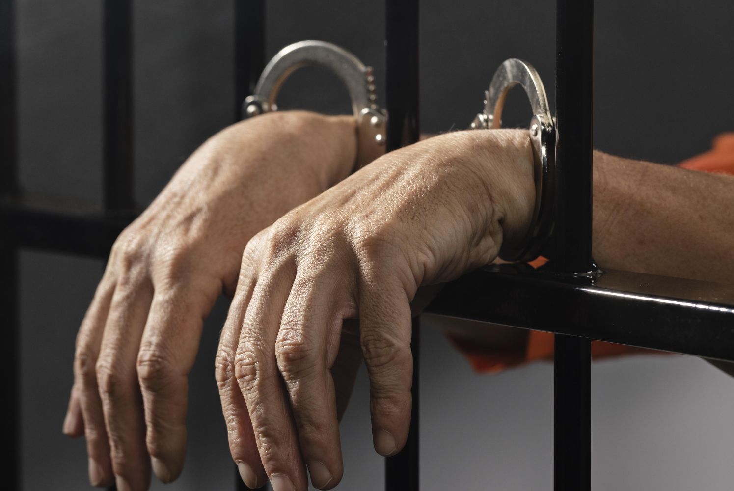 26dpenjara catrawarta Close up of a persons hands in metal handcuffs resting on jail bars conveying detention