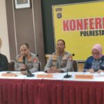Panel conference with three officials at a long table two police officers in uniform and a woman in hijab review documents Banner behind reads konferensi polresta yogyakarta