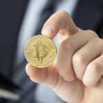 Businessperson in a suit holds a gold bitcoin coin toward the viewer