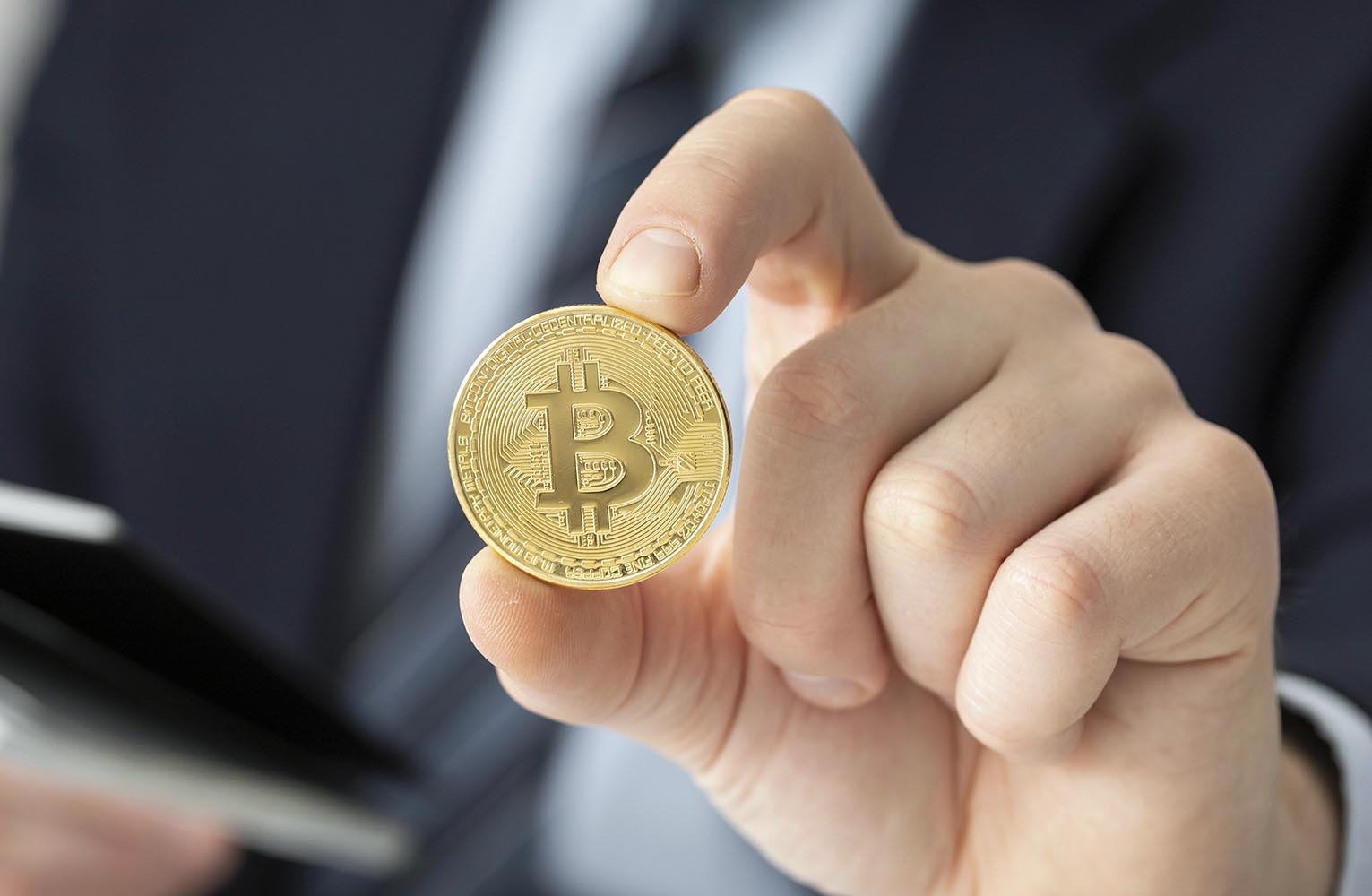 Businessperson in a suit holds a gold bitcoin coin toward the viewer