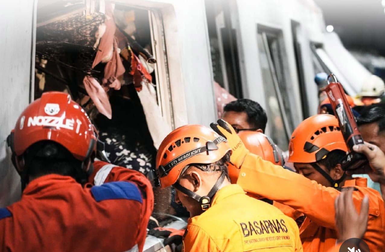 Emergency responders in orange uniforms and helmets extract passengers from a damaged train car amid debris during a rescue operation