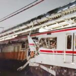 White commuter train with red stripes derailed against a platform front area severely damaged with bent metal and shattered windows