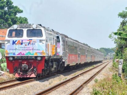 Diesel locomotive leading a long passenger train on a sunny rural railway through green countryside