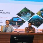 Panel discussion with three men seated at a conference table a presentation slide behind shows indonesian text and diamond shaped photos of rivers and coastlines