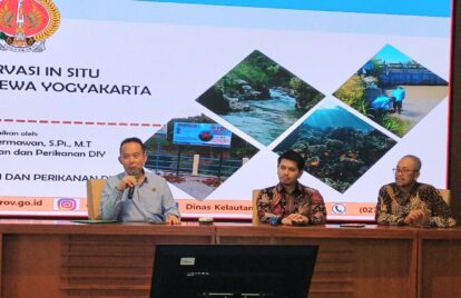 Panel discussion with three men seated at a conference table; a presentation slide behind shows Indonesian text and diamond-shaped photos of rivers and coastlines.