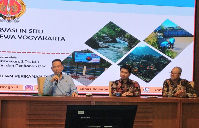 Panel discussion with three men seated at a conference table; a presentation slide behind shows Indonesian text and diamond-shaped photos of rivers and coastlines.