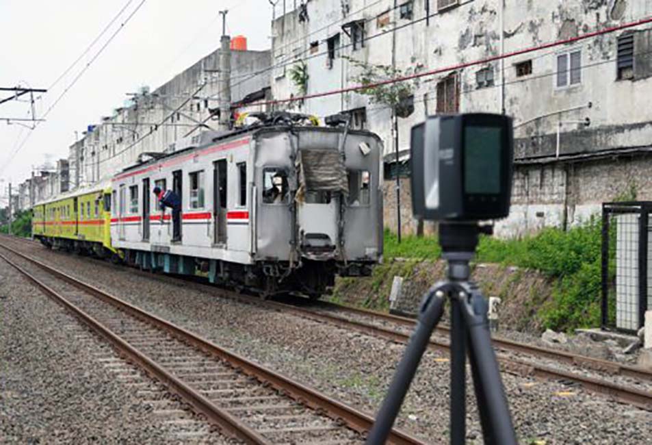 Damaged commuter train on tracks with peeling buildings in a city and a camera on a tripod in the foreground used for surveying