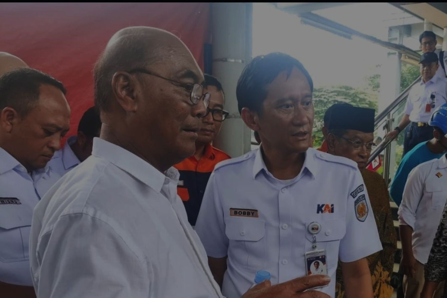 Group of men in white uniforms and name tags at a public event one badge reads bobby near an escalator