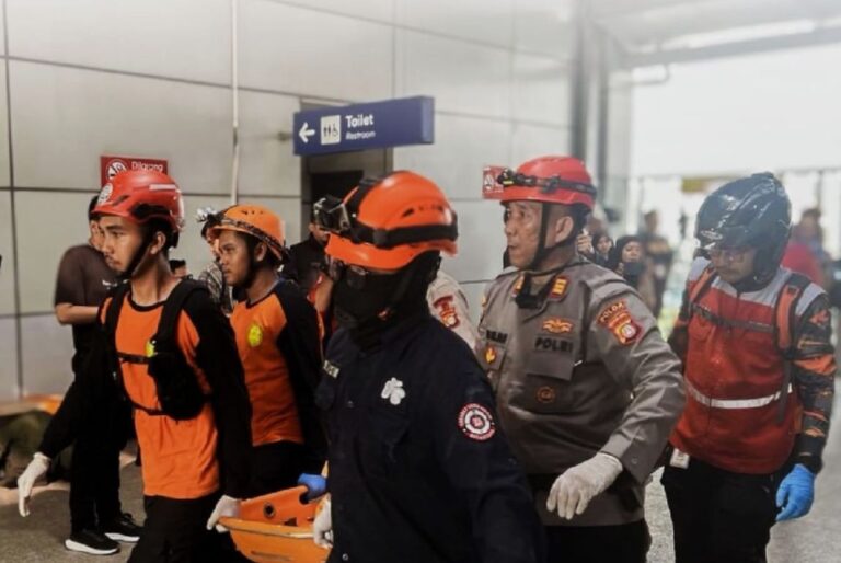 Emergency responders in orange vests and helmets escorting a person on a wheeled stretcher through a building corridor.