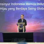 Man in a dark suit delivering a talk at a podium on a stage with a blue purple digital backdrop