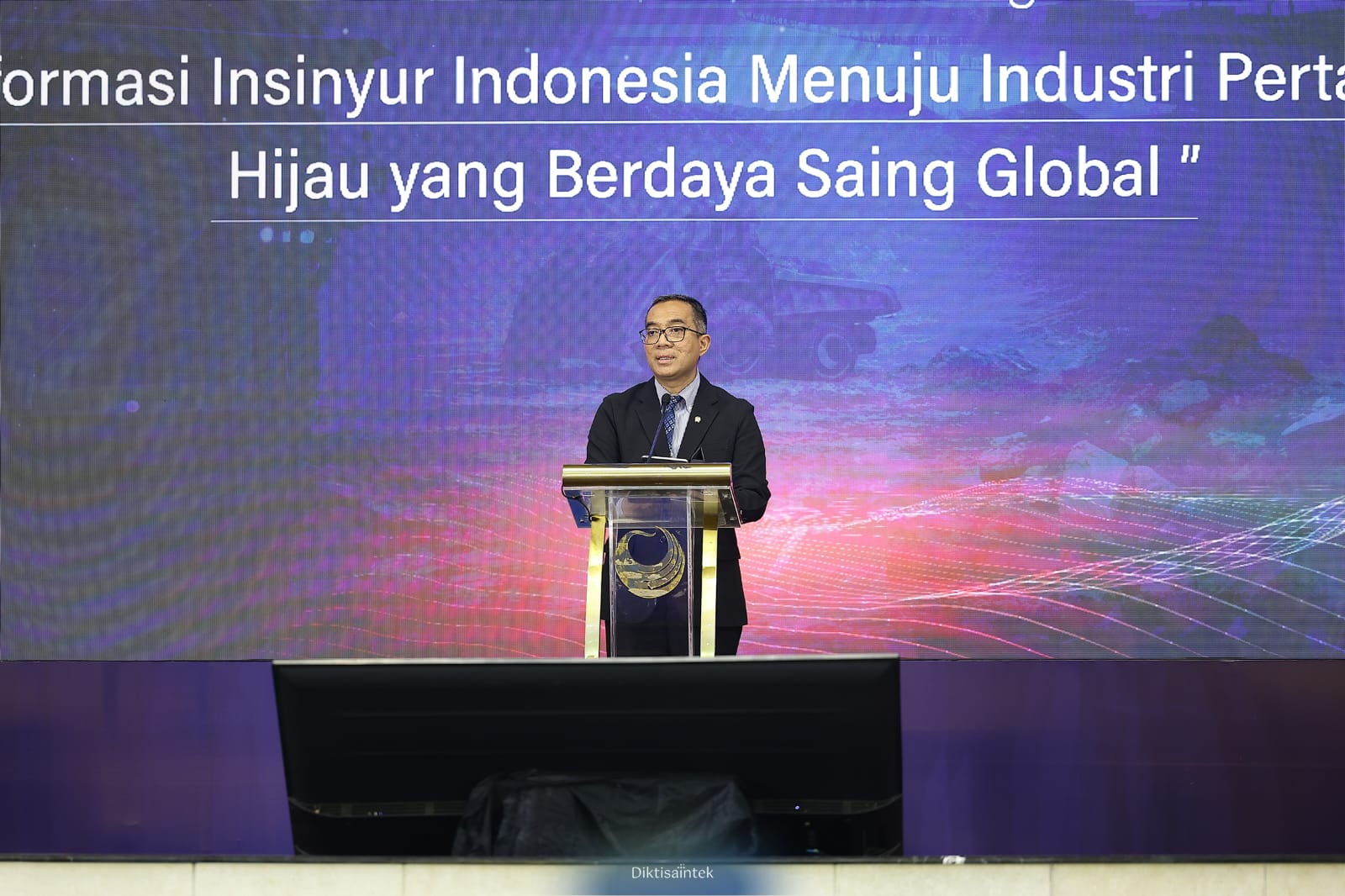Brian catrawarta Man in a dark suit delivering a talk at a podium on a stage with a blue purple digital backdrop