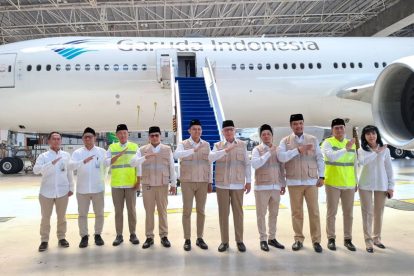 Group of Garuda Indonesia staff in uniforms posing in front of a plane inside a hangar.