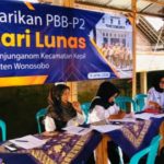 Registration desk for a 1 day tax payment event staff in hijabs assist attendees under a blue banner in indonesian