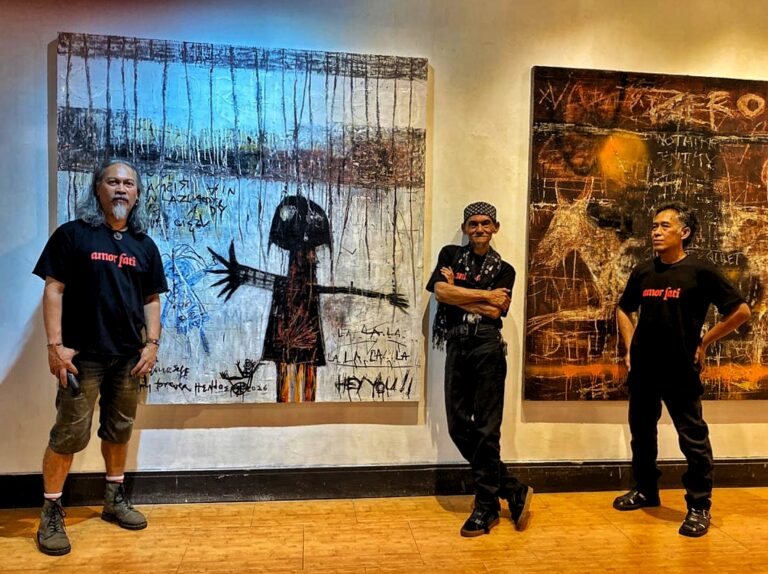 Three men in black shirts stand in front of two large abstract paintings in a gallery setting.