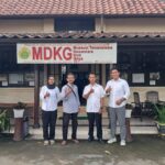 Four adults pose and give thumbs up in front of a museum entrance with a large mdkg banner reading museum tamansiswa in yogyakarta