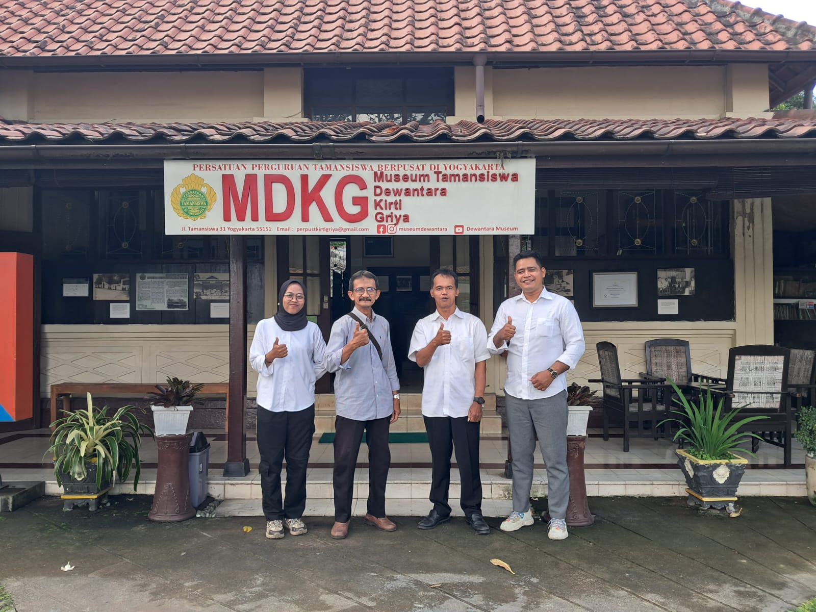 Img20260430wa0016 catrawarta Four adults pose and give thumbs up in front of a museum entrance with a large mdkg banner reading museum tamansiswa in yogyakarta
