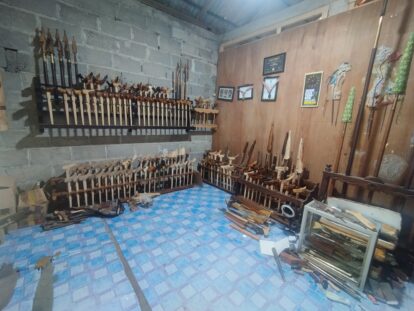 Workshop wall with rows of wooden-handled carving chisels and knives on metal racks against a concrete block wall.
