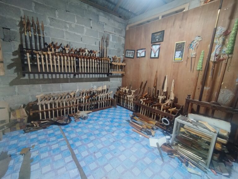 Workshop wall with rows of wooden-handled carving chisels and knives on metal racks against a concrete block wall.