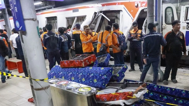People in orange vests stand near a stopped train on a platform some examining the doorway nearby