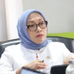 Woman in a light blue hijab and glasses sits at a conference table looking thoughtful during a meeting