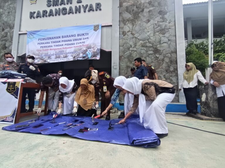 Officials and civilians destroy seized items on a blue tarp outside a police building during a evidence destruction event.