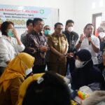 Group of officials and healthcare workers at a free health check event banner reading cek kesehatan gratis in the background