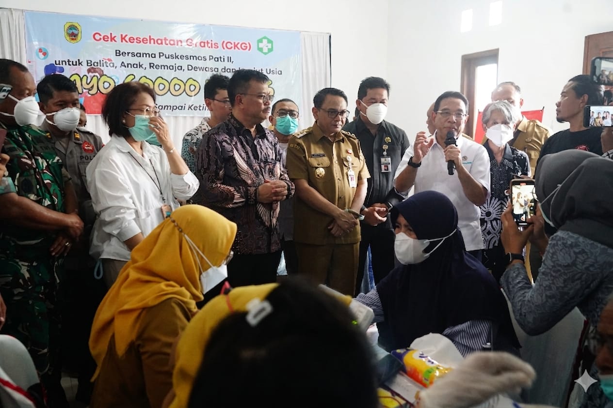 Group of officials and healthcare workers at a free health check event banner reading cek kesehatan gratis in the background