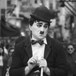 Mime street performer with white face makeup bowler hat dark suit and cane in a crowded city street