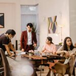 Group of coworkers in a bright lounge discussing documents around a glass conference table mid meeting